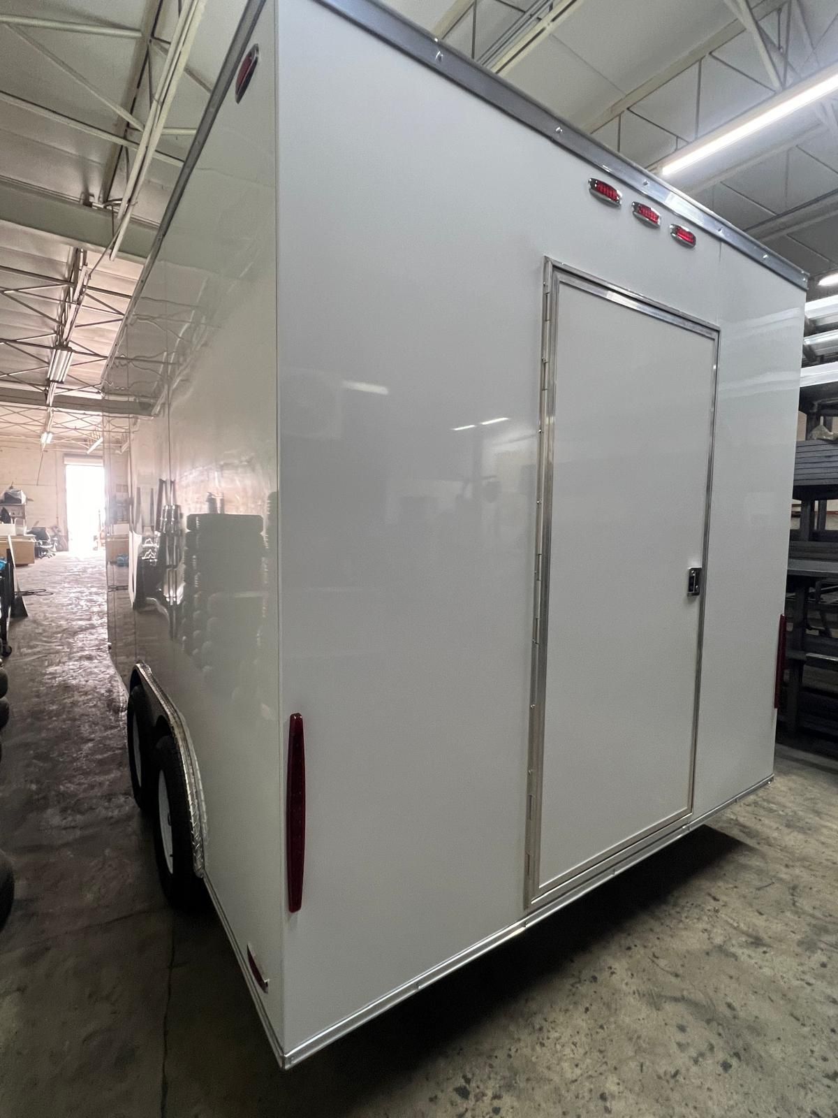White enclosed cargo trailer in a warehouse, with side door and red marker lights.