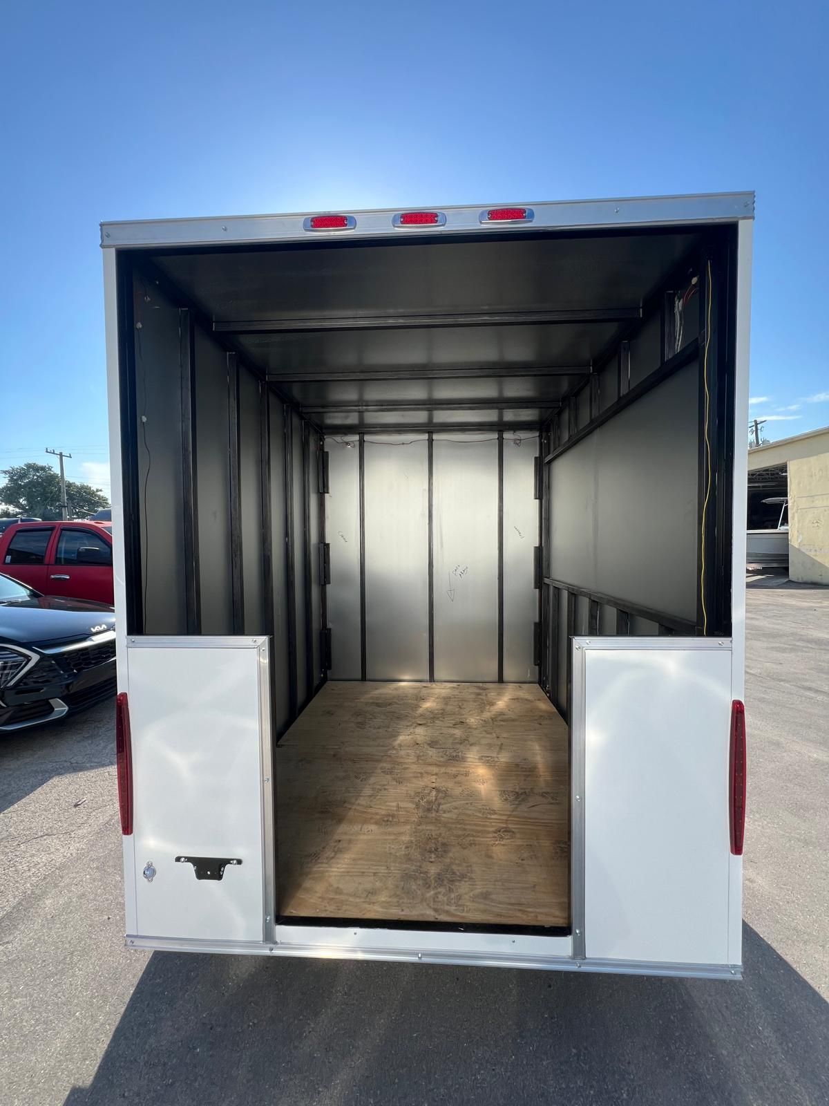 Open white cargo trailer with empty interior and rear doors open on a parking lot