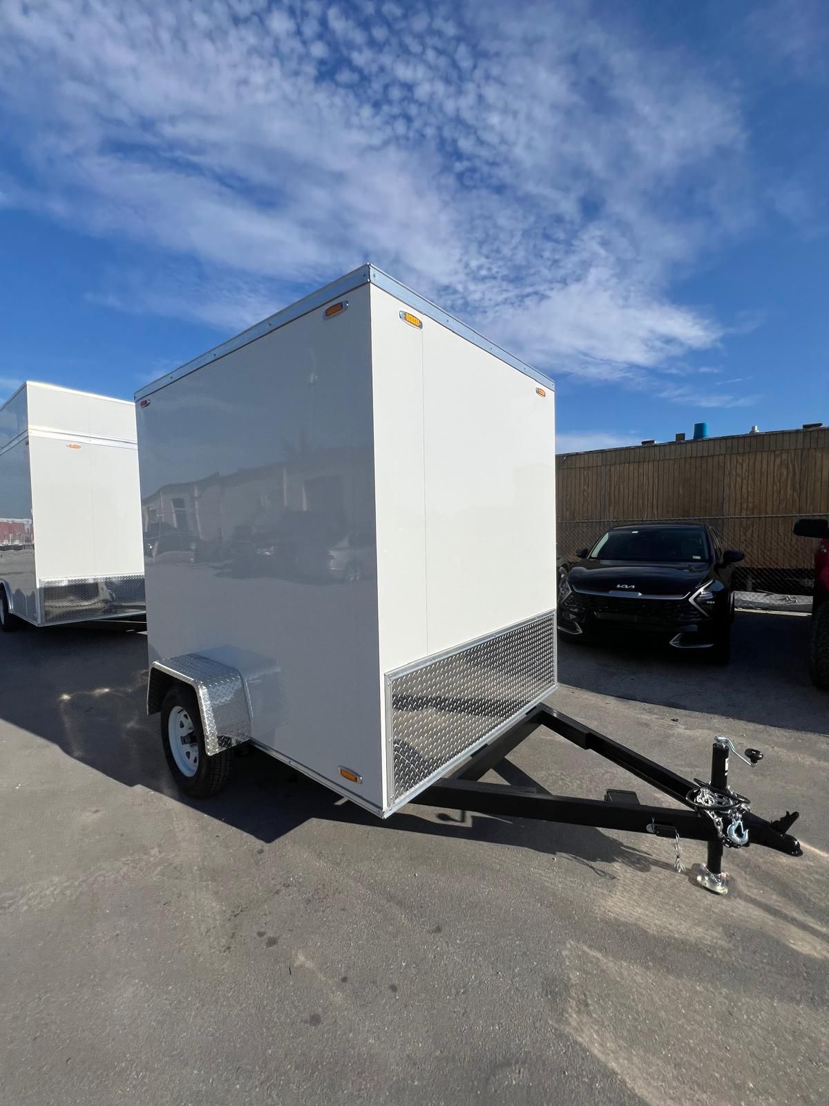White enclosed cargo trailer with ramp on a parking lot under a blue sky