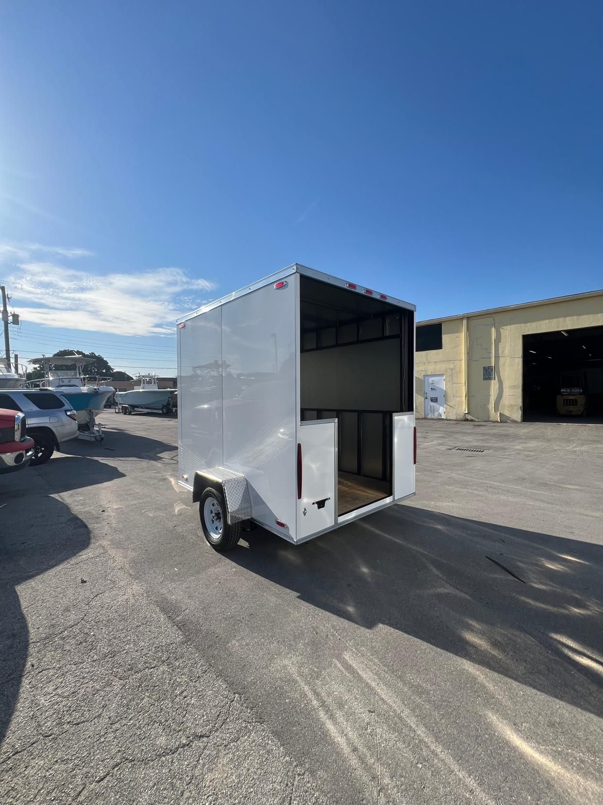 White enclosed cargo trailer with open rear doors parked on a sunny lot.