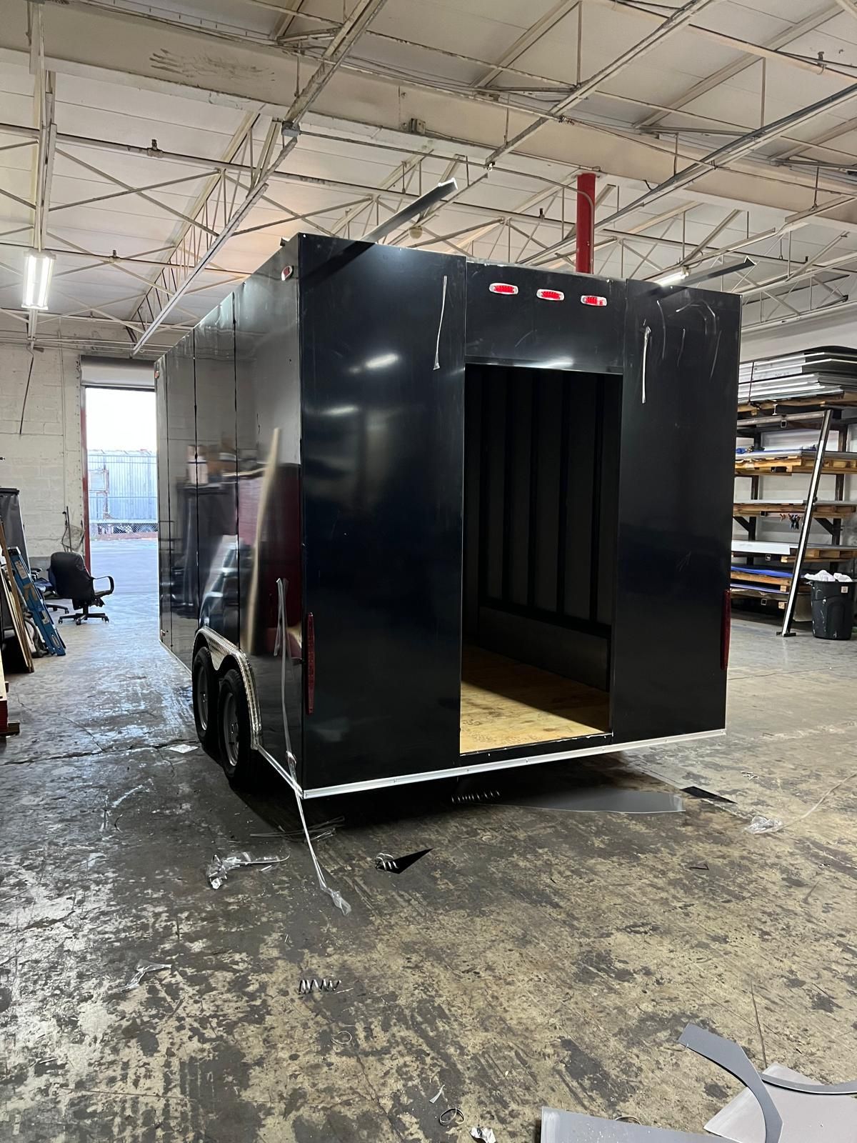 Black box-like trailer or booth in a workshop, with an open doorway and shelves in the background