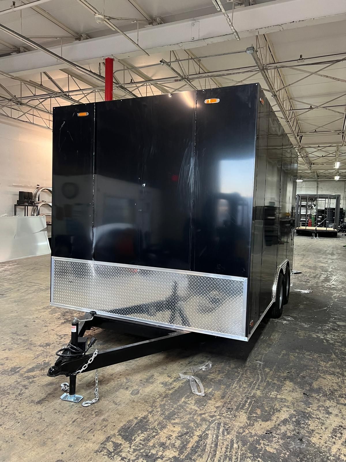 Black enclosed trailer with silver diamond-plate lower panel in an indoor warehouse, hitched to a tow bar