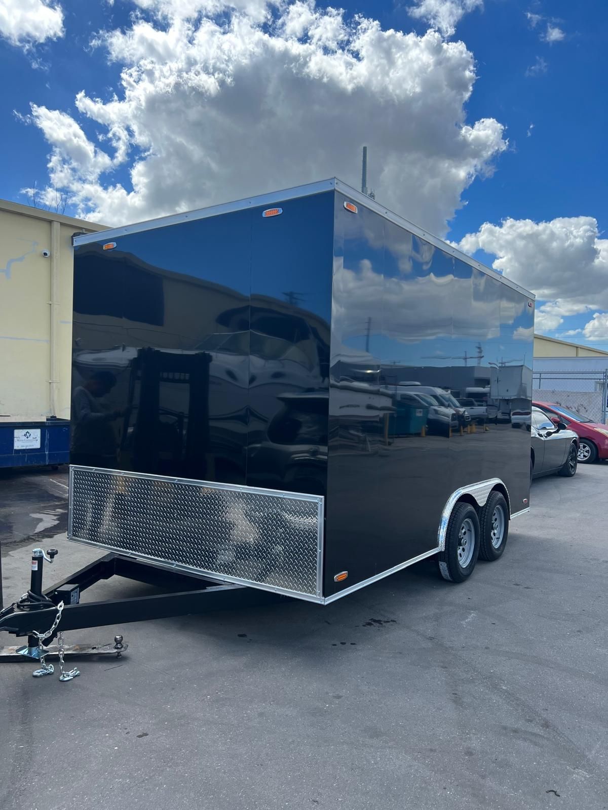 Black enclosed dual-axle cargo trailer with chrome lower panels parked in a lot under a cloudy sky
