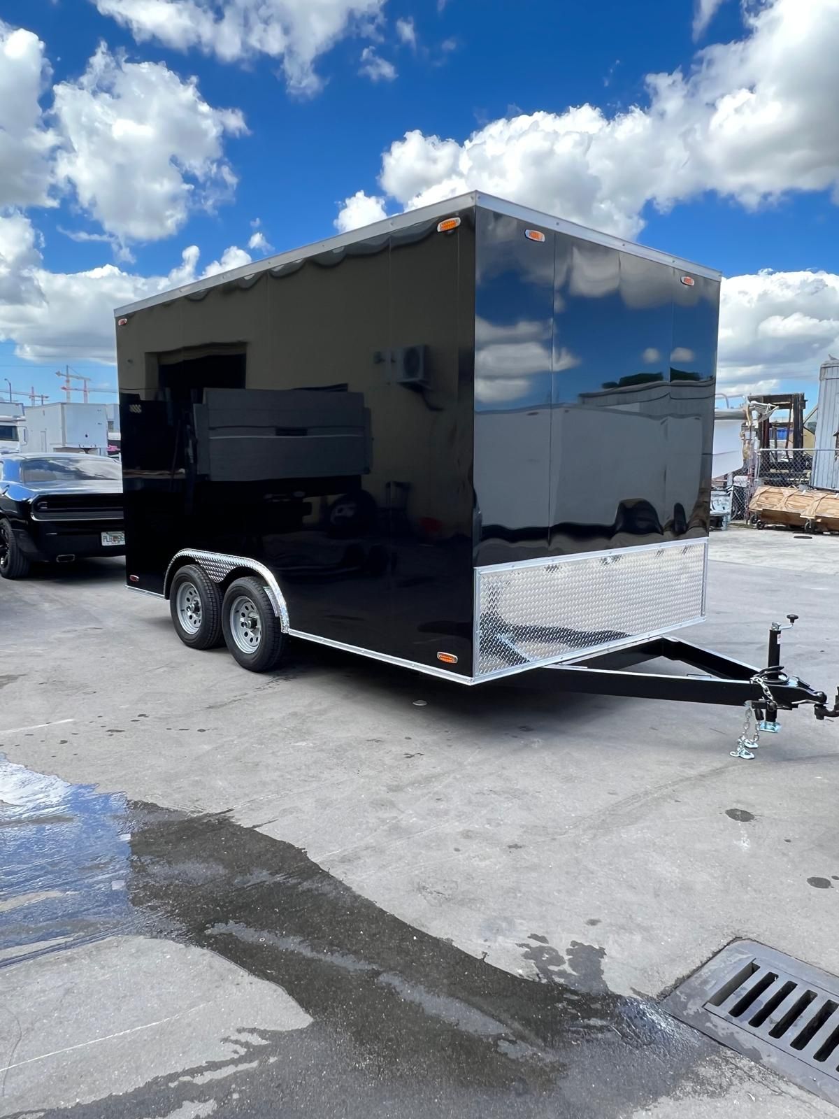 Black enclosed cargo trailer parked on a lot under a cloudy sky.