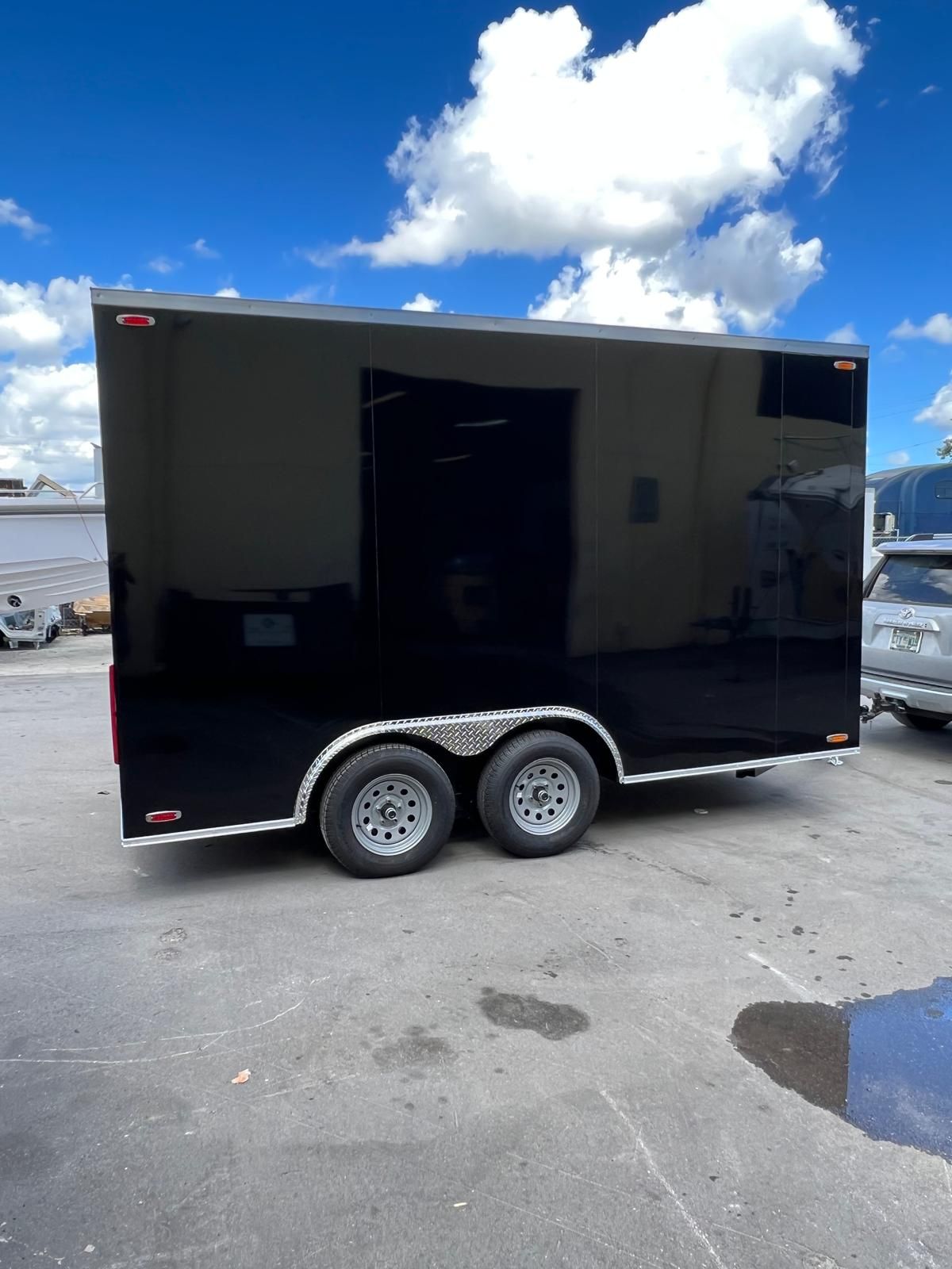 Black dual-axle enclosed cargo trailer parked on pavement under a blue sky.