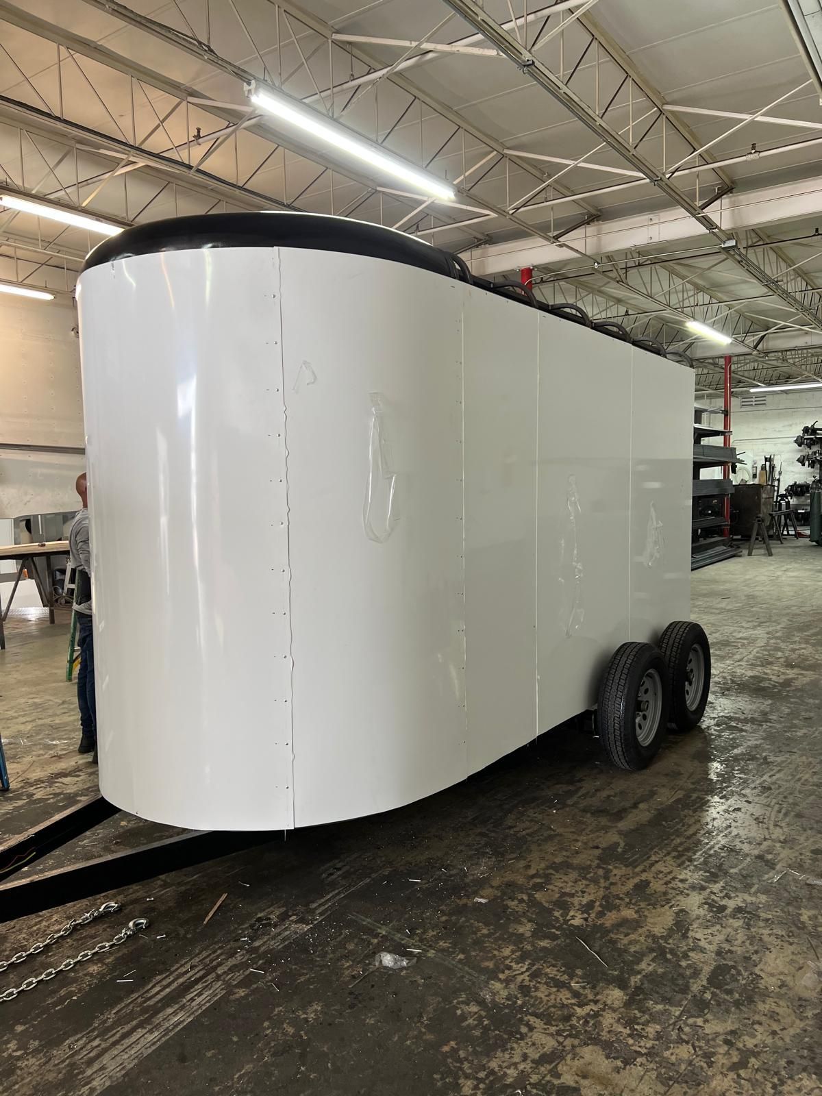 White enclosed cargo trailer with black trim and dual axles inside a warehouse.