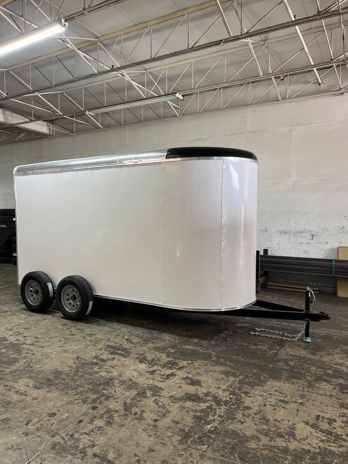 White enclosed cargo trailer with dual axles parked indoors in a warehouse.