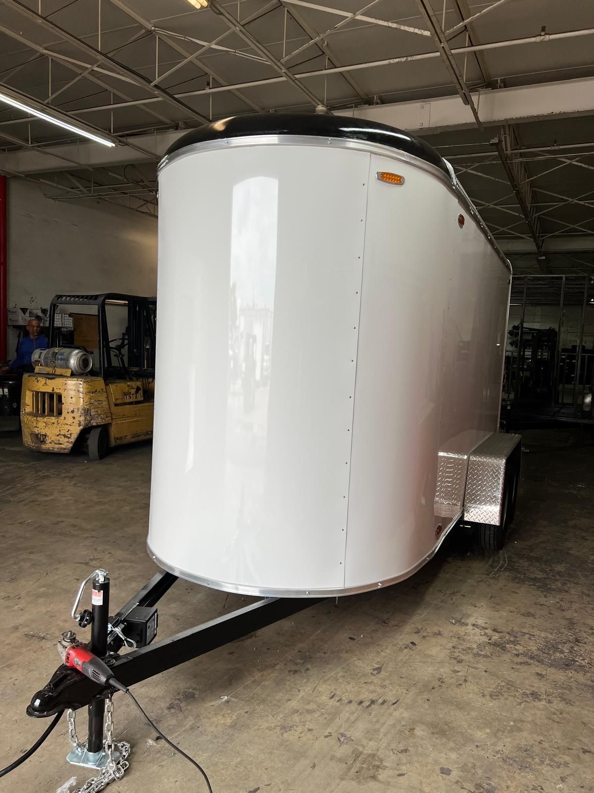 White enclosed trailer in a warehouse, with black trim and a trailer hitch in the foreground.