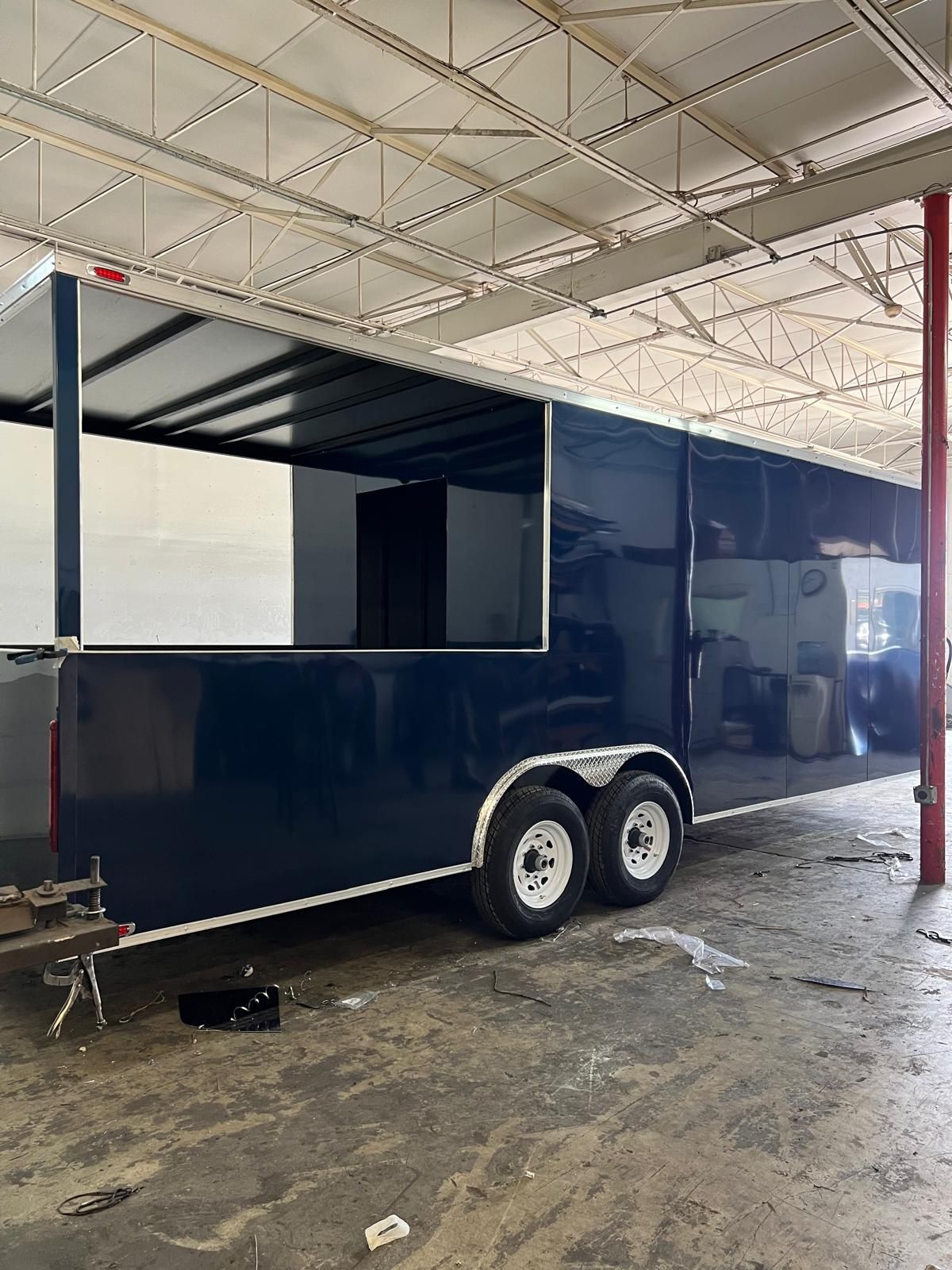 Black enclosed trailer with two axles parked under a covered industrial shed.