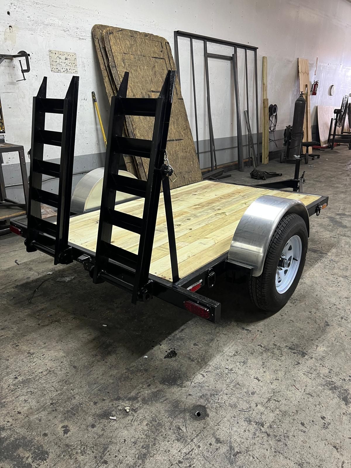Small utility trailer with wooden floor and black metal frame in a workshop garage.