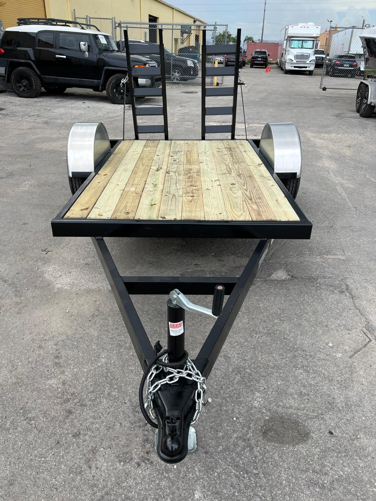 Utility trailer with wood deck, black frame, and hitch in an industrial lot
