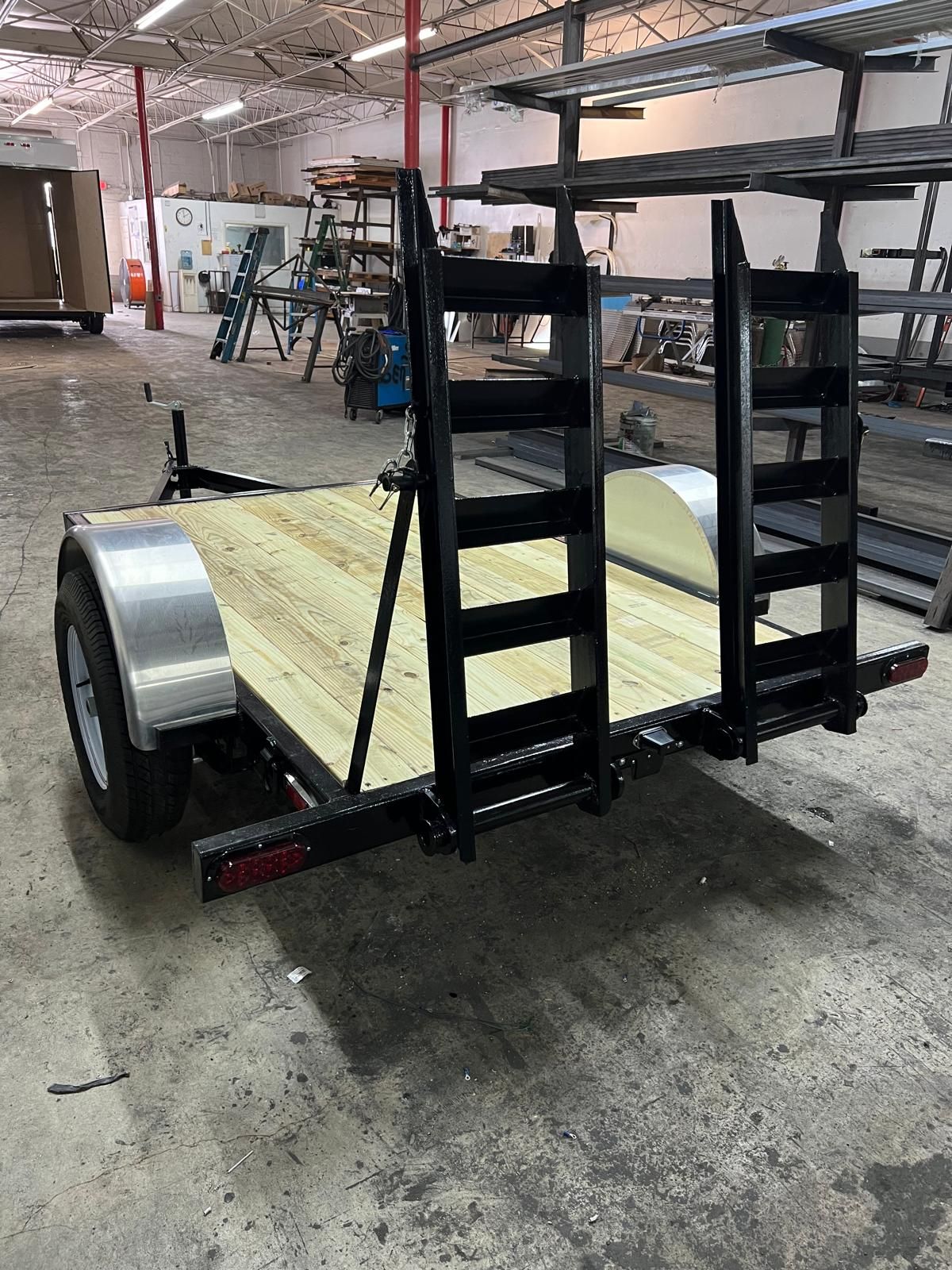 Small flatbed utility trailer with black racks and wood deck in a warehouse.