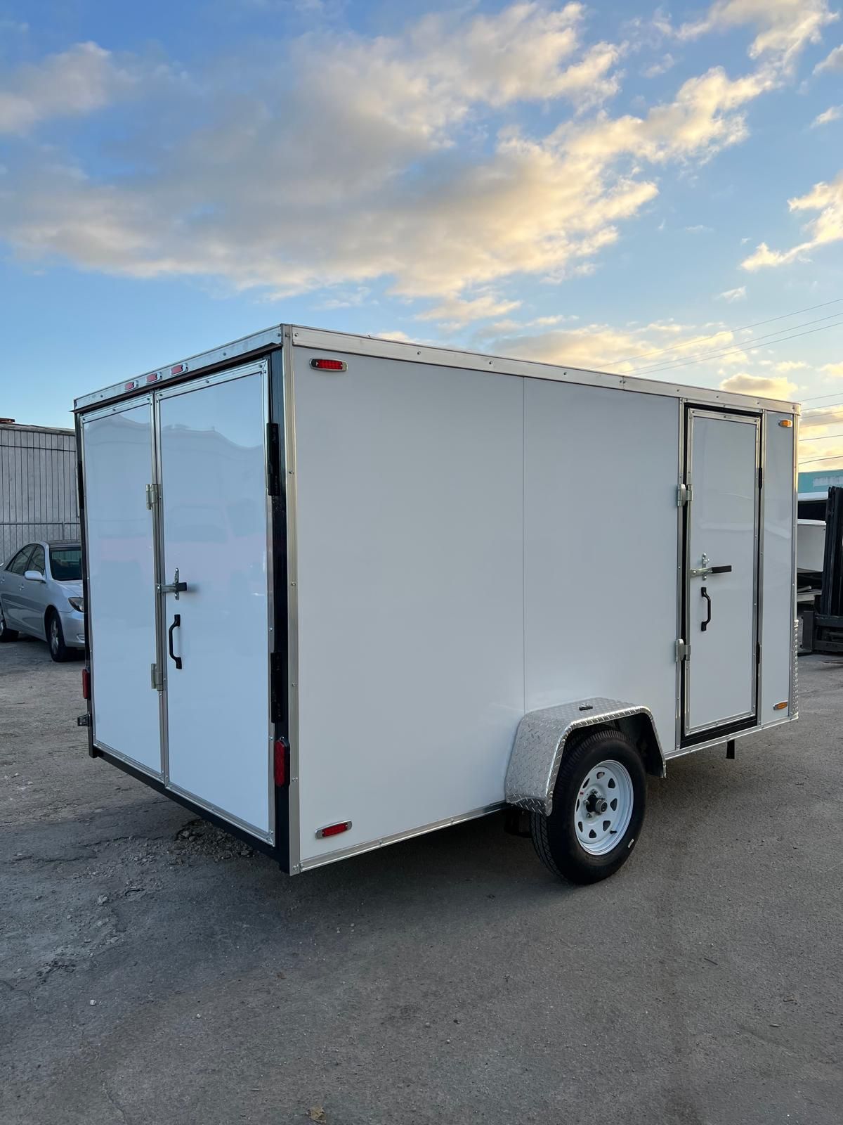 White enclosed cargo trailer parked outdoors on asphalt under a cloudy sky