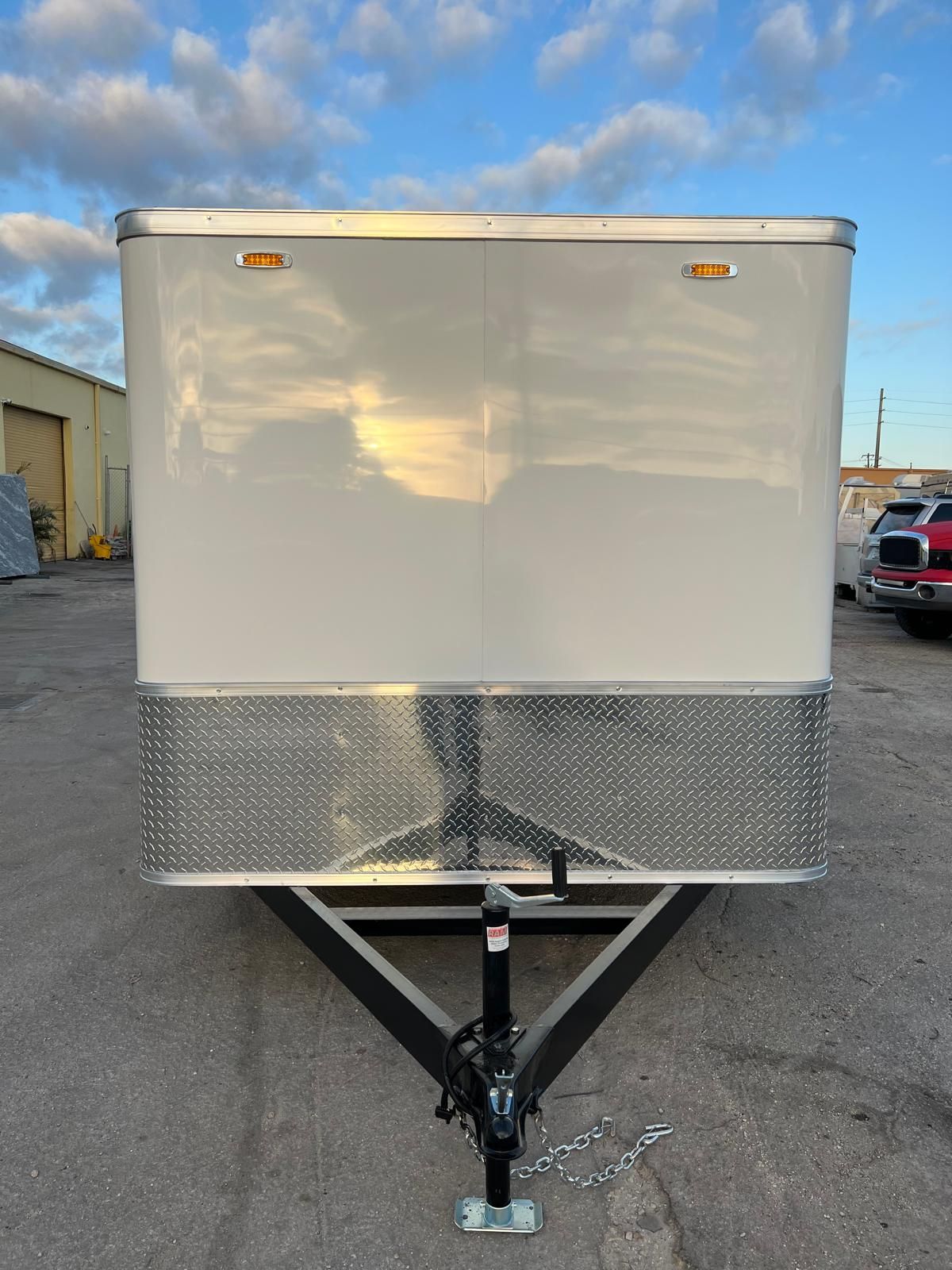 White enclosed utility trailer parked outdoors on a gravel lot, front view.