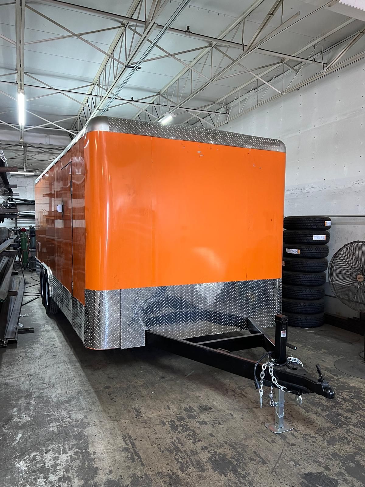Orange enclosed trailer in a workshop, with silver trim and a hitch in the foreground.