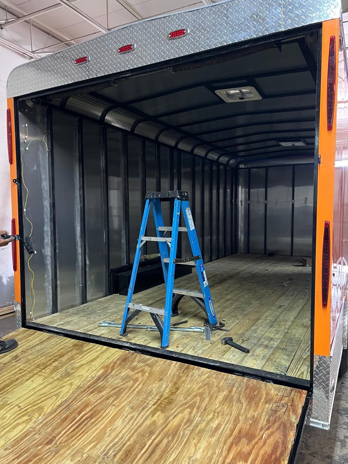 Blue step ladder inside an empty black cargo trailer with an orange frame and wood floor.