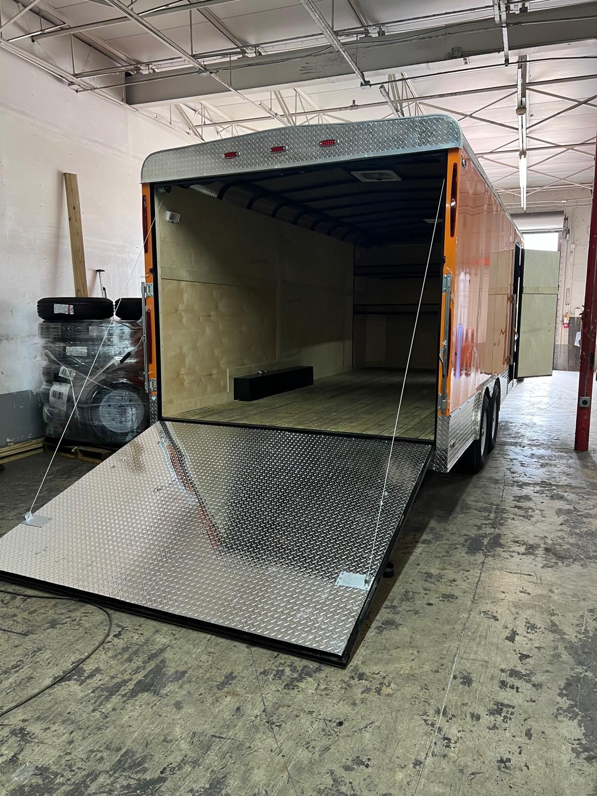 Open trailer with metal ramp lowered in a warehouse workspace