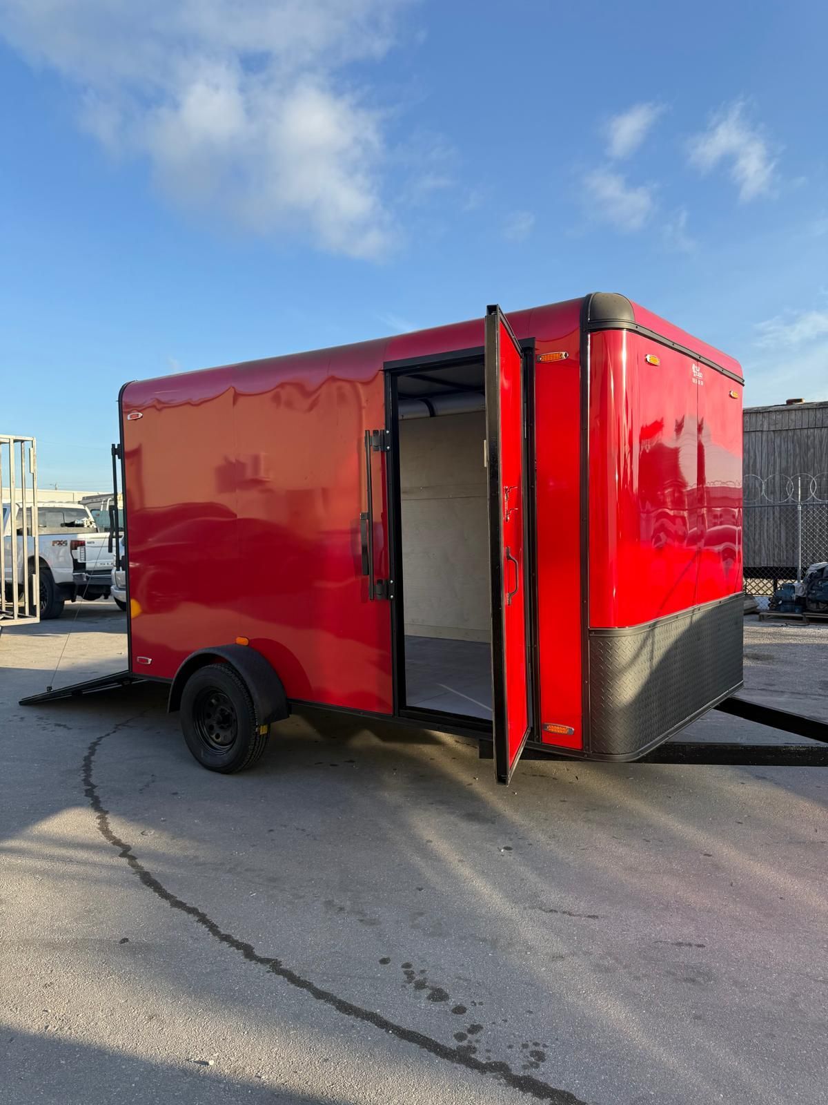 Red enclosed utility trailer with open door parked on pavement under a blue sky.