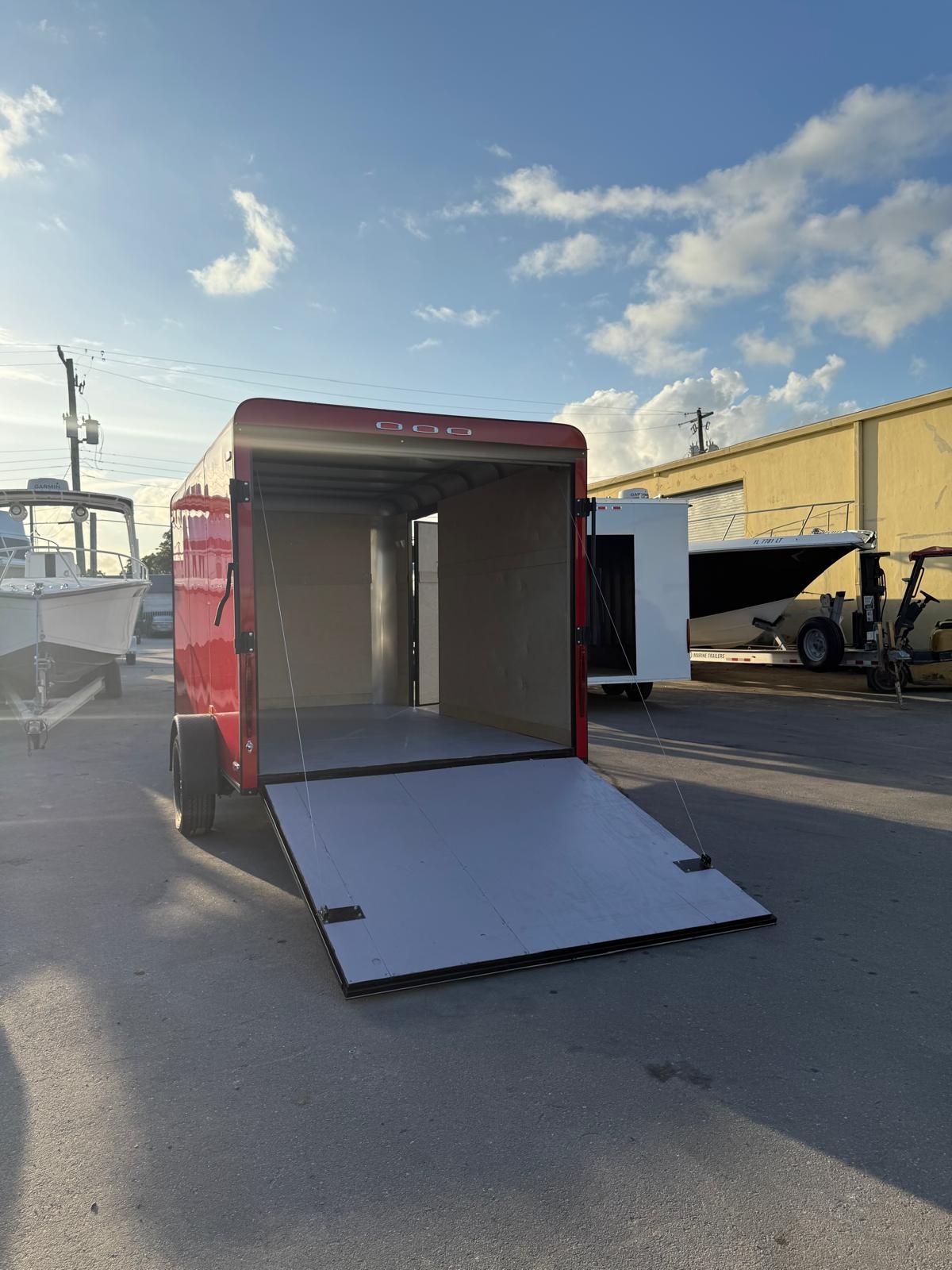 Red enclosed cargo trailer with lowered ramp door in an outdoor lot at sunset