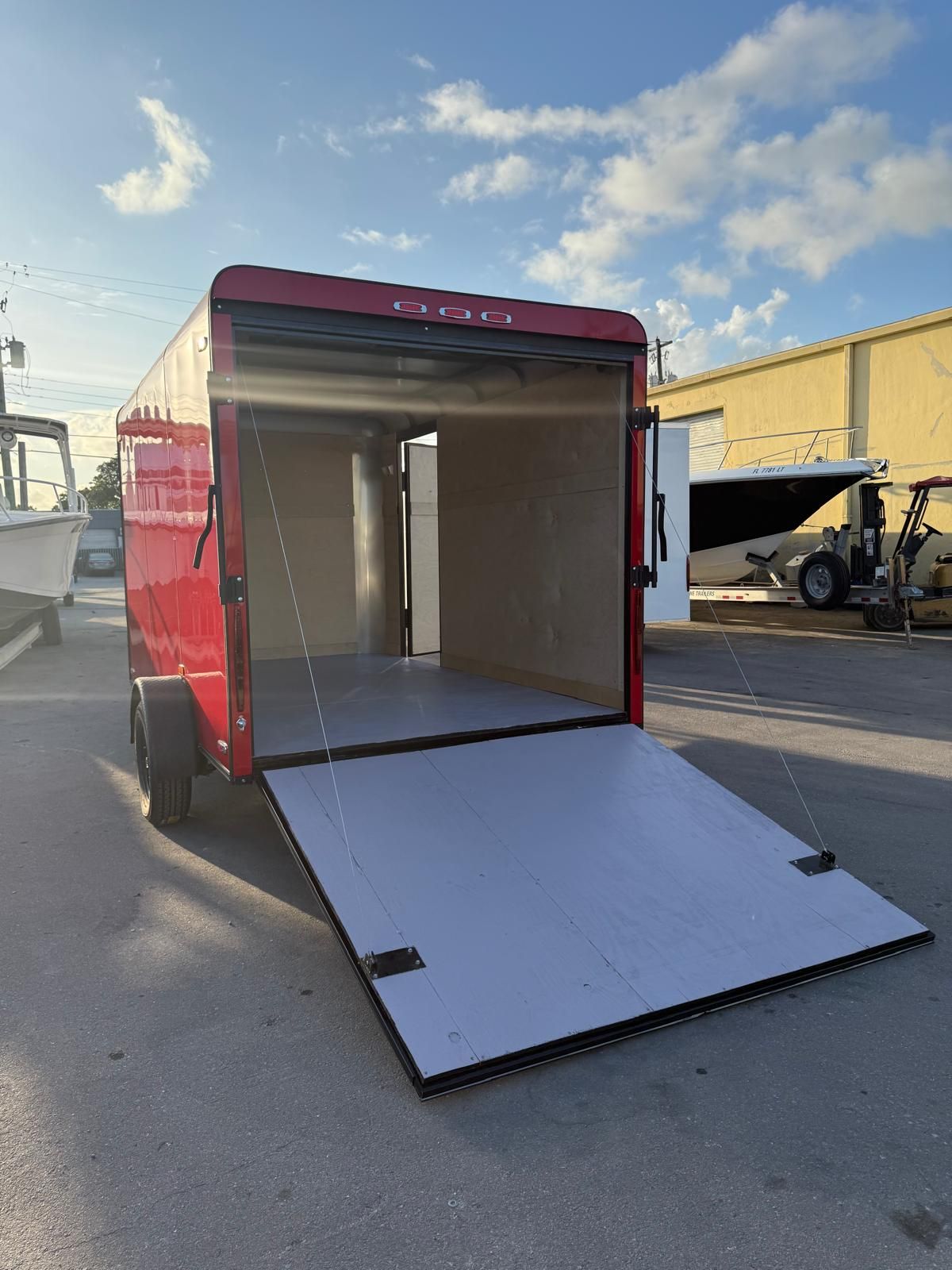 Red box trailer with open rear ramp in an outdoor industrial lot under a blue sky