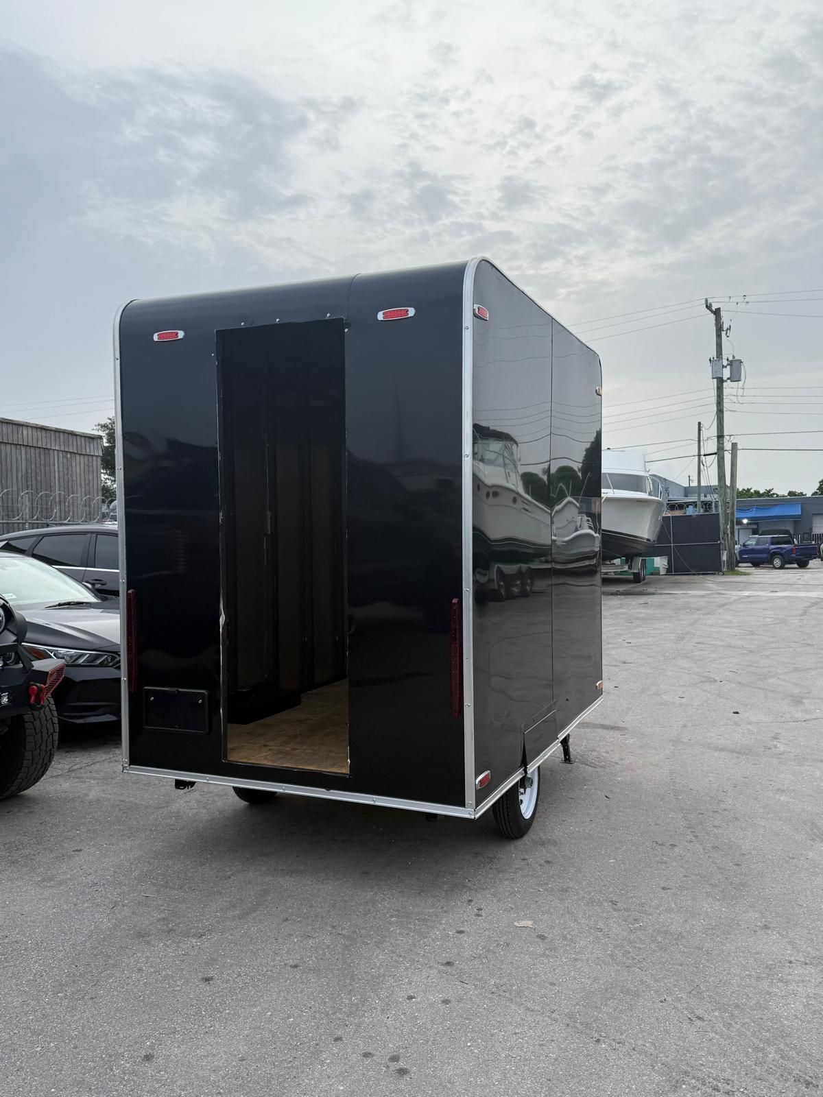 Black enclosed cargo trailer with open rear door parked in an industrial lot