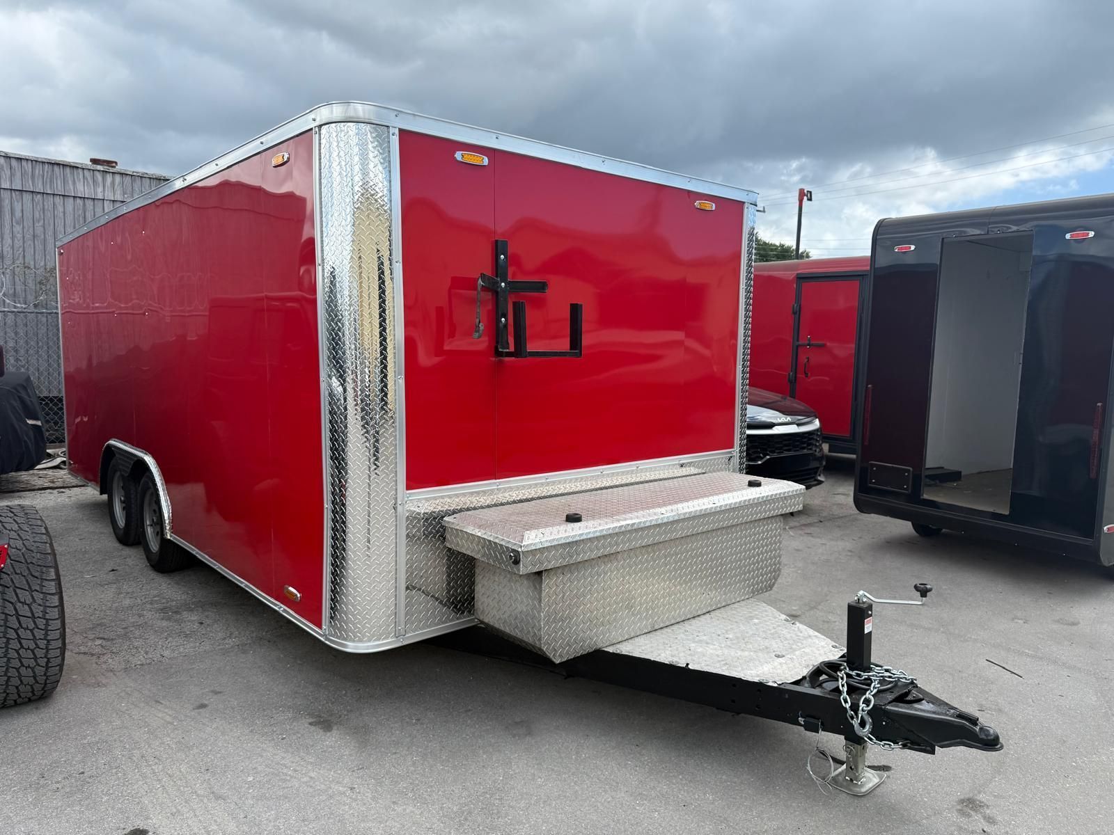Red enclosed cargo trailer with silver trim and hitch parked on a lot.