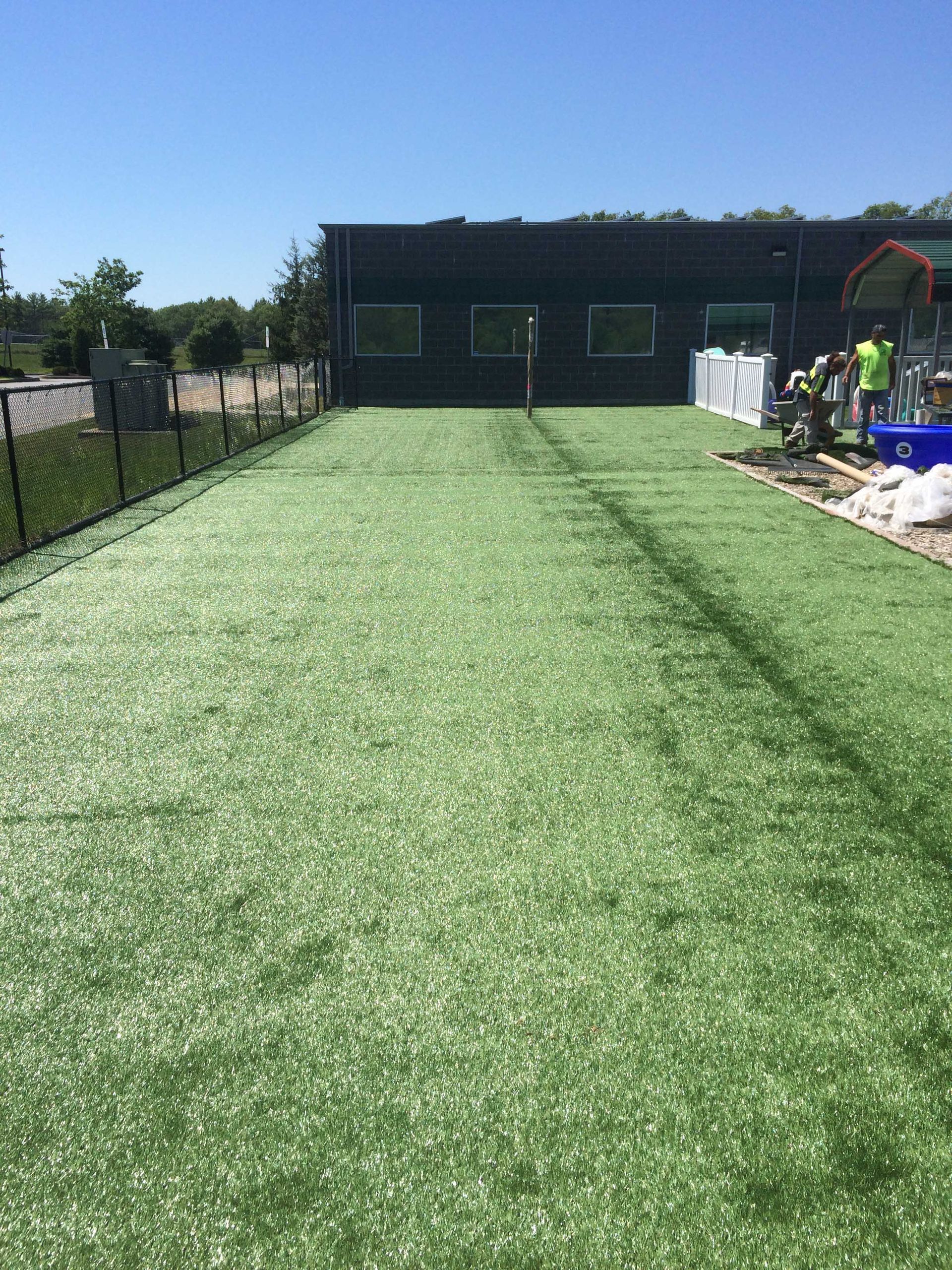 A long strip of newly installed artificial grass leading up to a dark building under a bright blue sky.