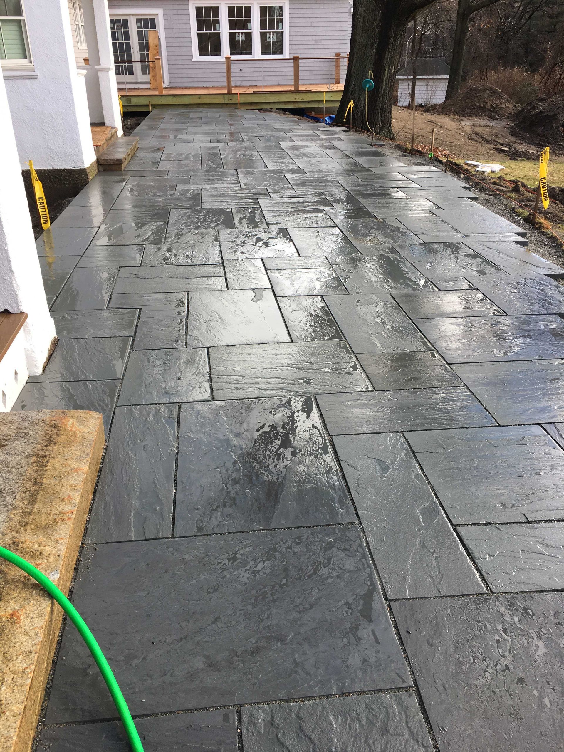 A newly laid gray stone patio extending from a house, wet from recent rain.
