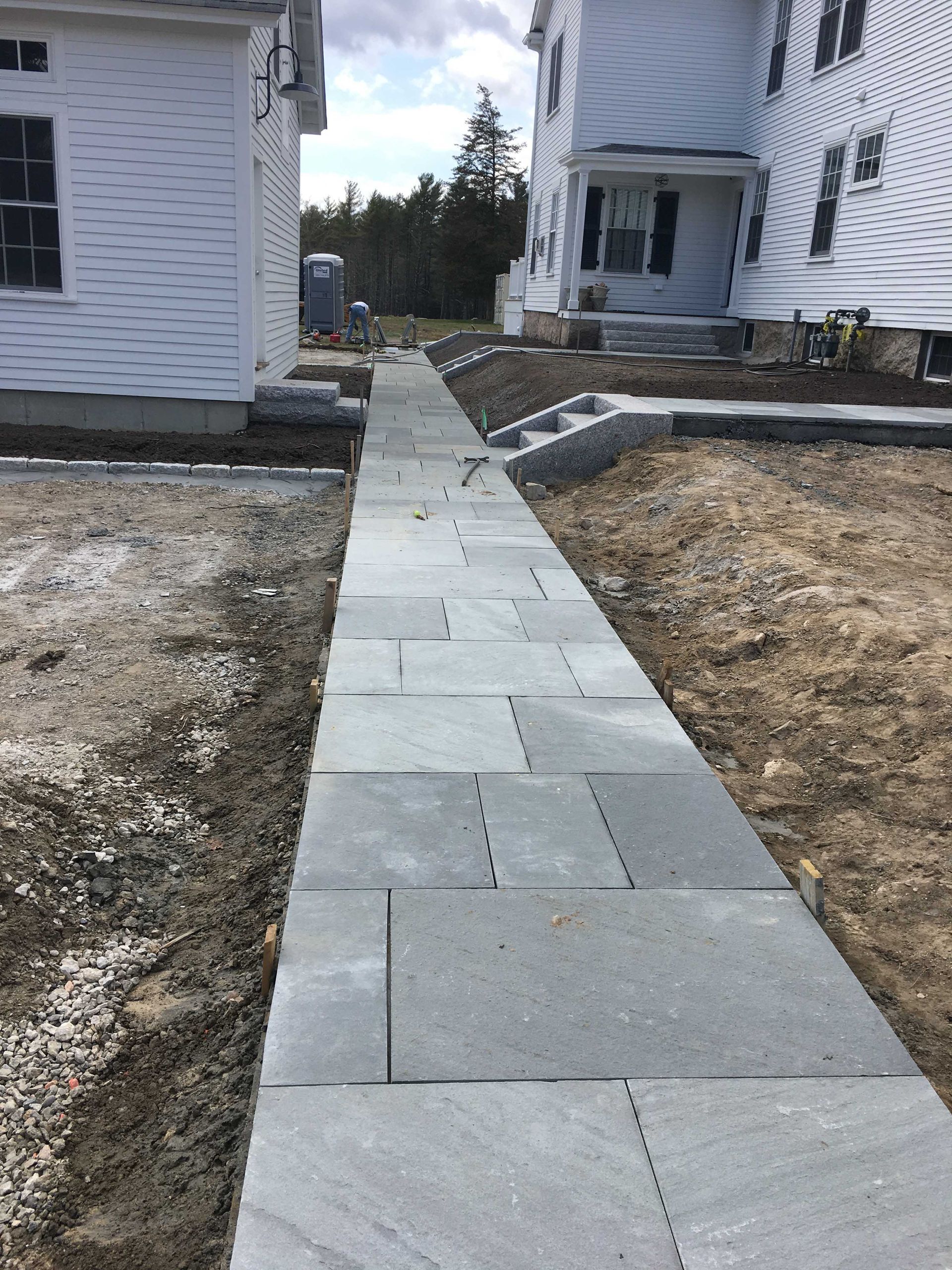 A stone walkway stretches between two white houses under a partly cloudy sky.