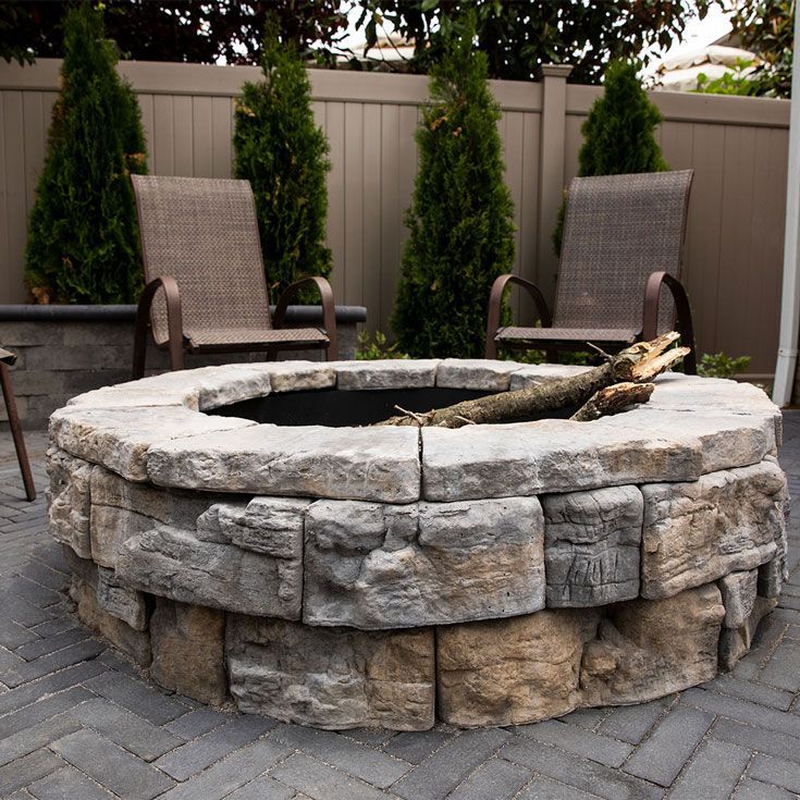 A fire pit is surrounded by chairs and a fence