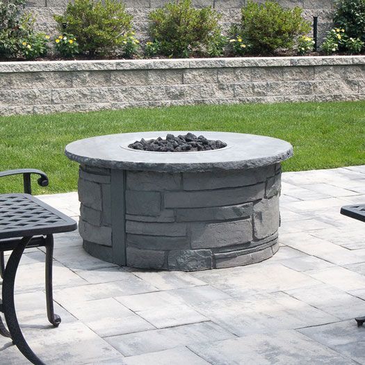 A fire pit is sitting on a patio next to a table and chairs.