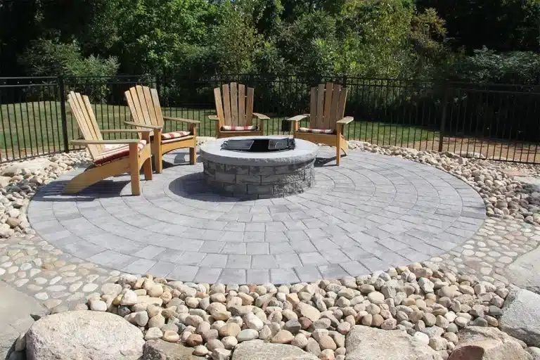 A fire pit in the middle of a patio with chairs around it.