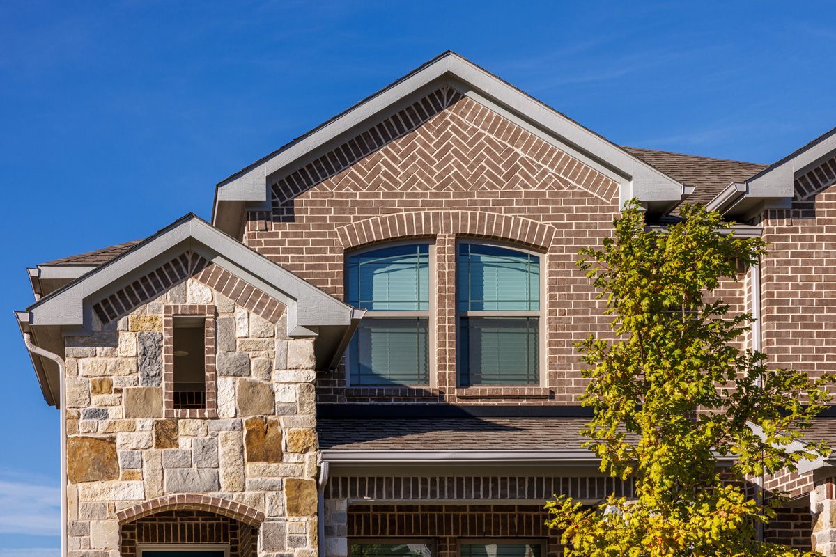 Two-story brick and stone house facade with gabled roof and blue-trimmed windows under a clear sky