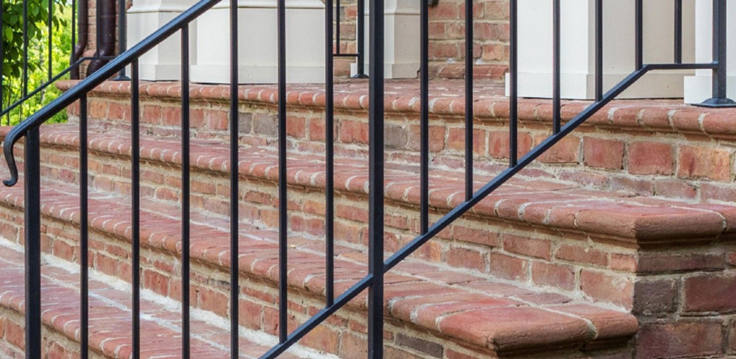 Brick front steps with black metal railing beside a building entrance