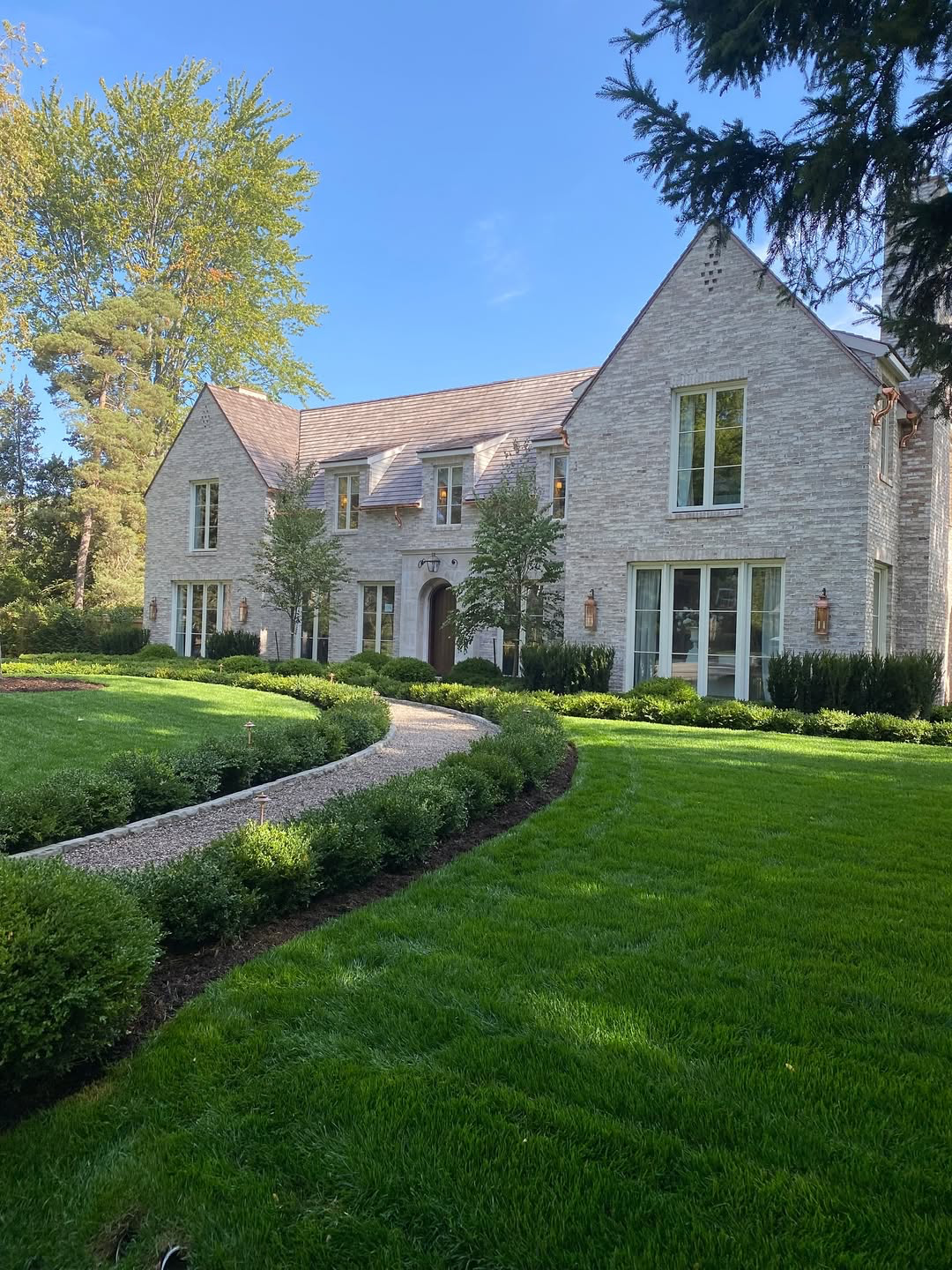 Large stone house with a curved garden path, green lawn, and bright blue sky