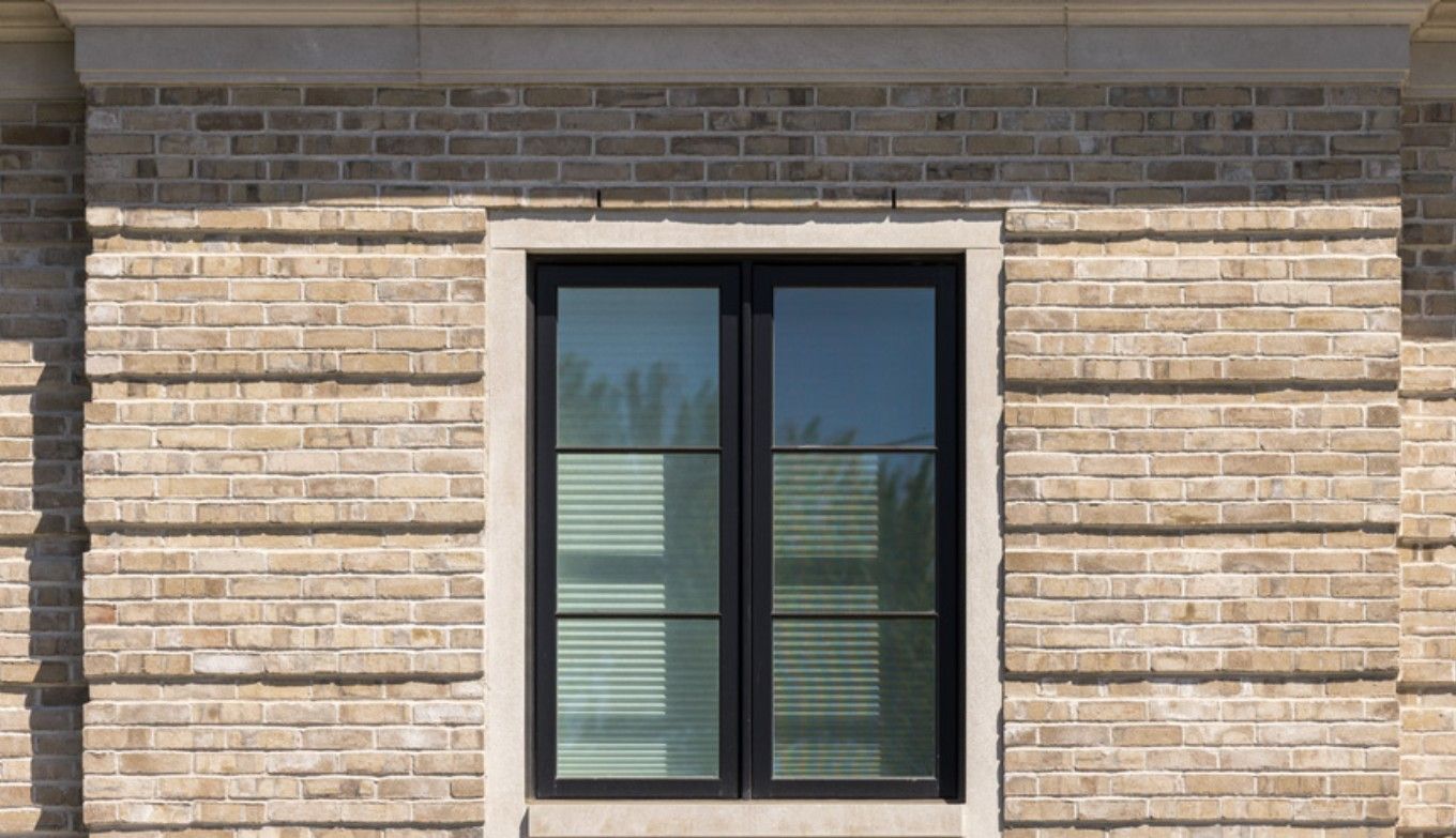 Black-framed window set in a tan brick wall with horizontal blinds behind the glass