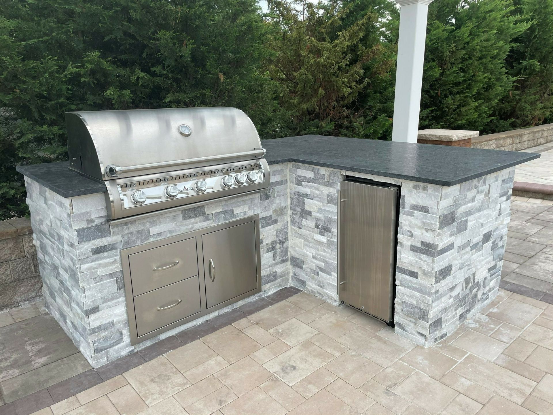An outdoor kitchen with a grill and a refrigerator.