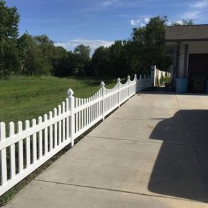 White picket fence along a driveway, next to a grassy area under a blue sky.