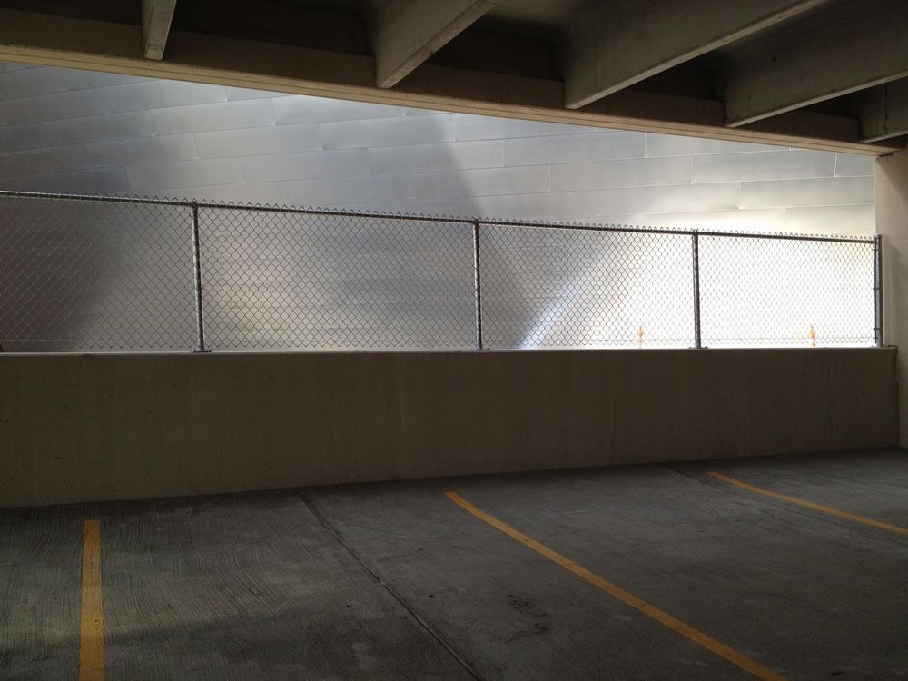 Parking garage interior with chain-link fence on a concrete wall. Bright sunlight through the fence.