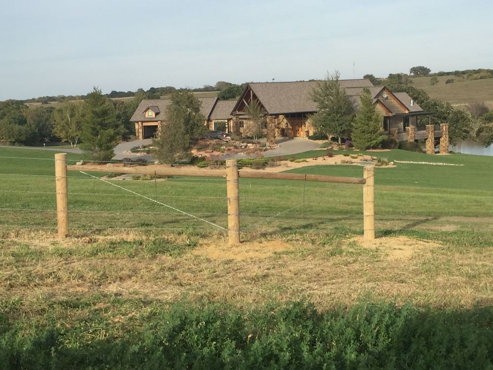 Wooden fence in a grassy field with a large house in the background.