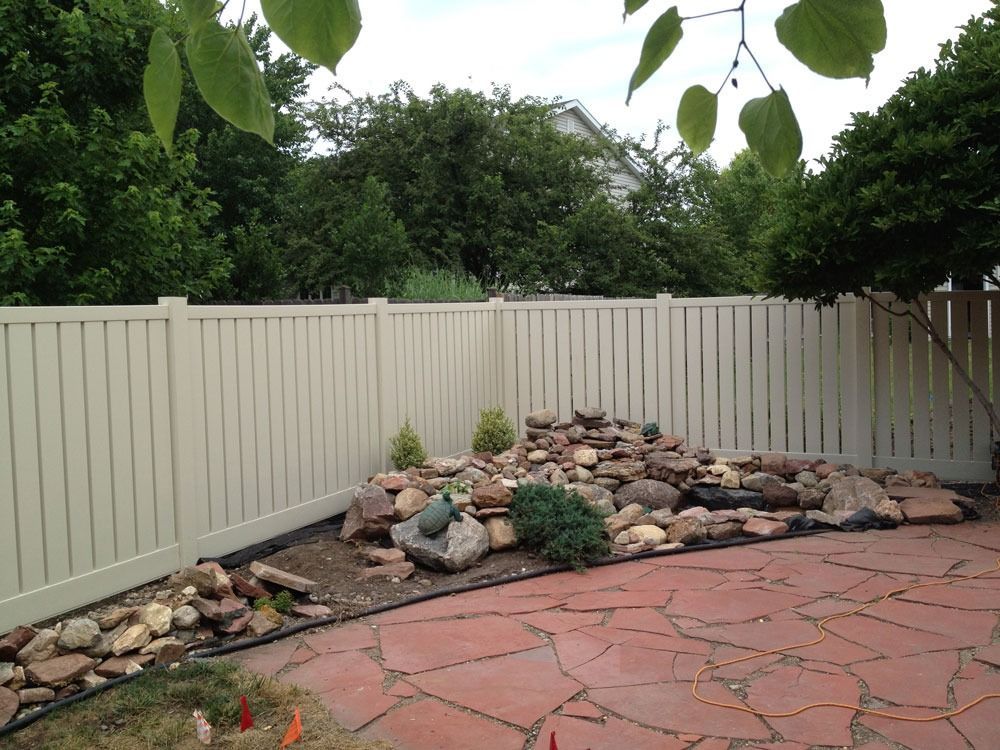 Backyard patio with beige fence, stone waterfall feature, and flagstone paving.