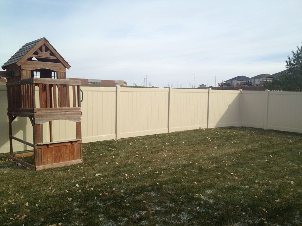 Play structure in a fenced backyard with grass and cloudy sky.
