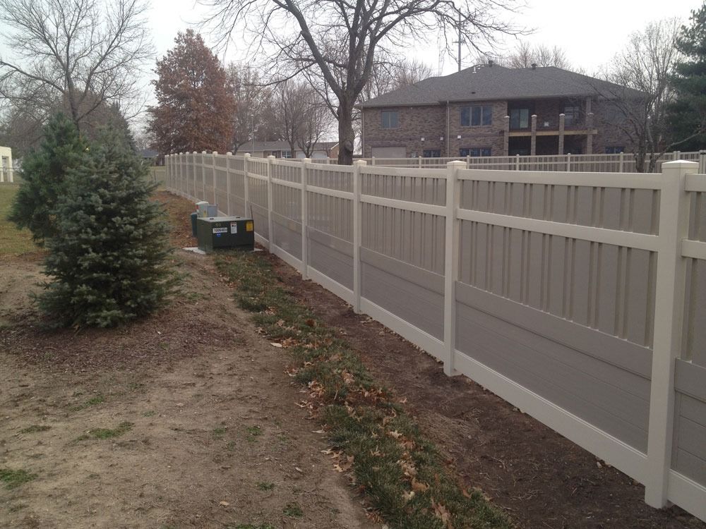 Tan and white vinyl fence runs alongside a yard with a small evergreen tree.