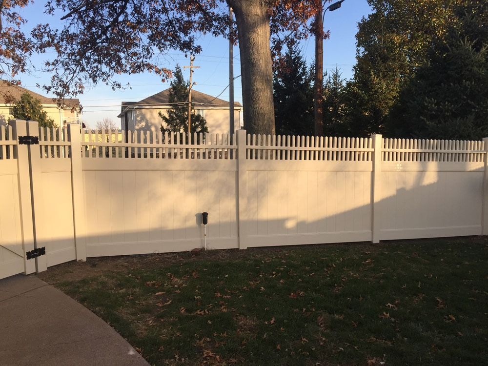 White vinyl fence enclosing a grassy yard, with a house visible in the background.