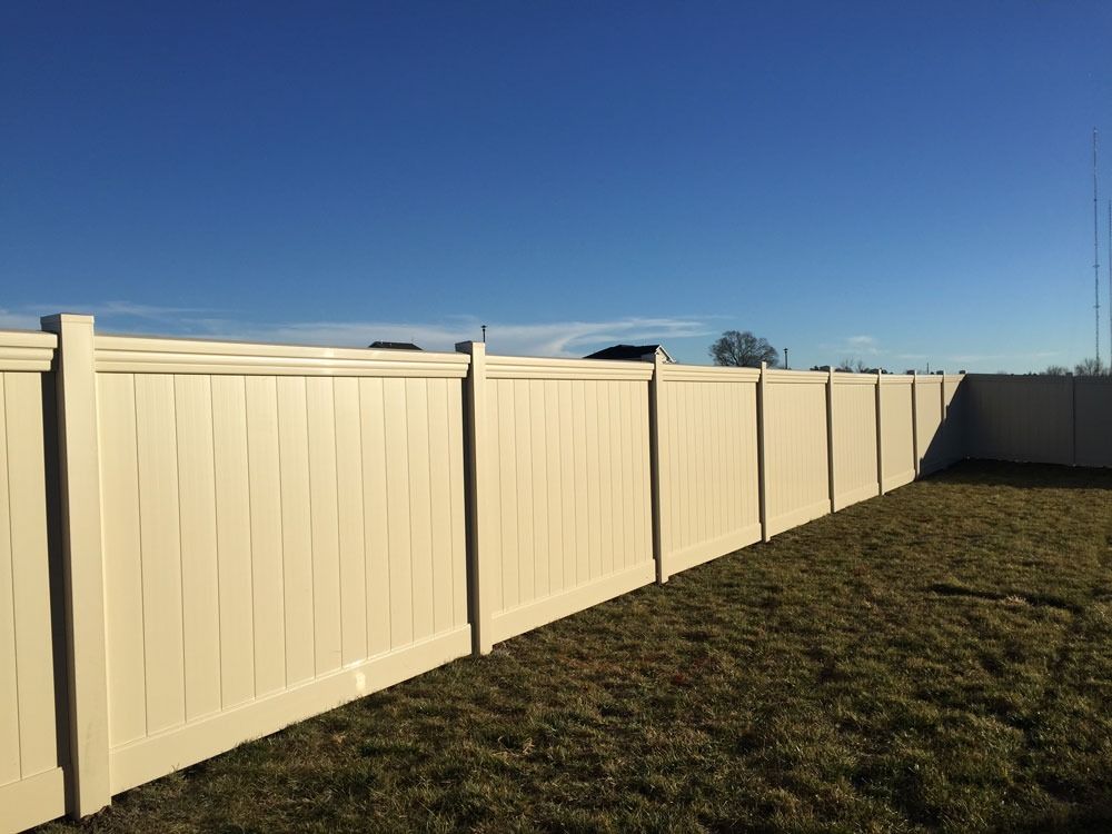 Tan vinyl fence in a grassy yard against a clear blue sky.