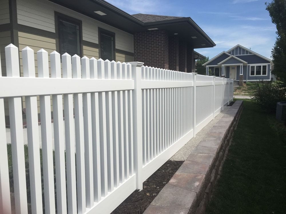 White picket fence bordering a brick and beige house and a blue house.