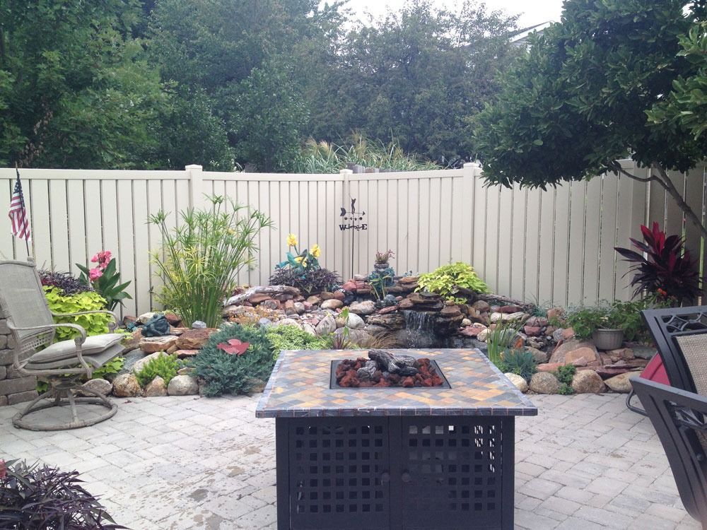 Patio with fire pit, pond with waterfall, and a white fence.