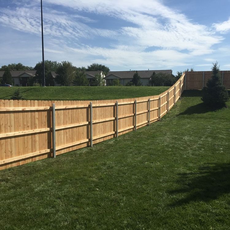 Wooden fence surrounding a grassy yard under a blue sky with some clouds.