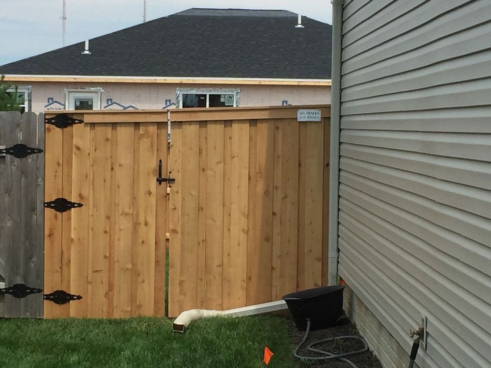 Wooden gate in a backyard, beside a house with tan siding and a dark roof.