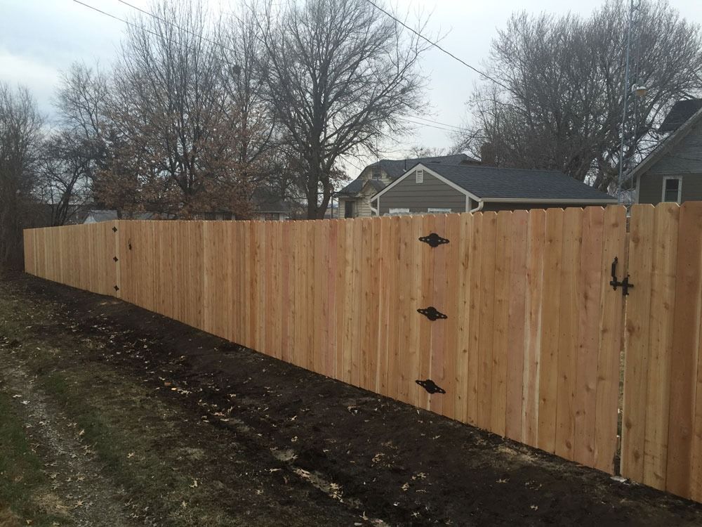 Wooden fence along a dirt path, with trees and houses in the background.